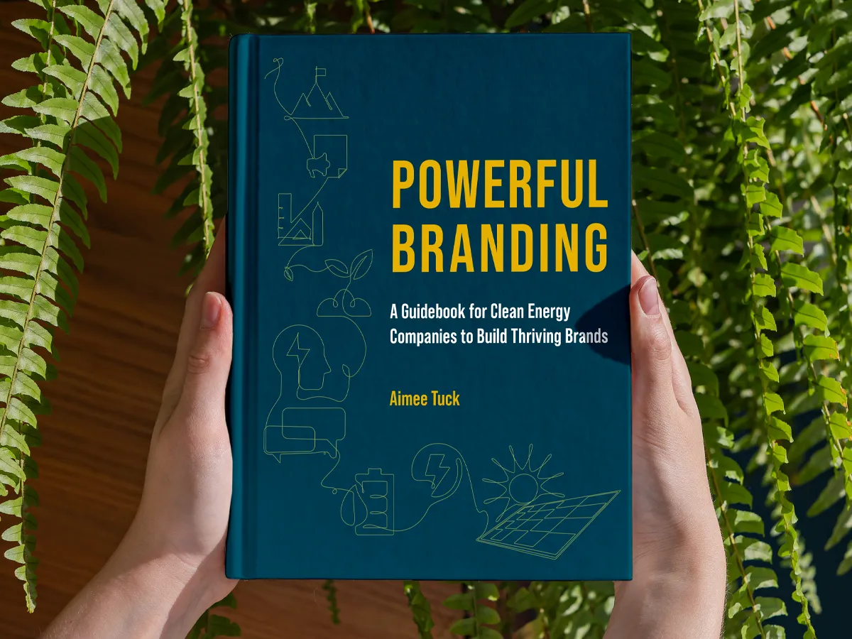 Front cover of Powerful Branding, A Guidebook for Clean Energy Companies to Build Thriving Brands by Aimee Tuck. The book is held in two hands with green ferns in the background.